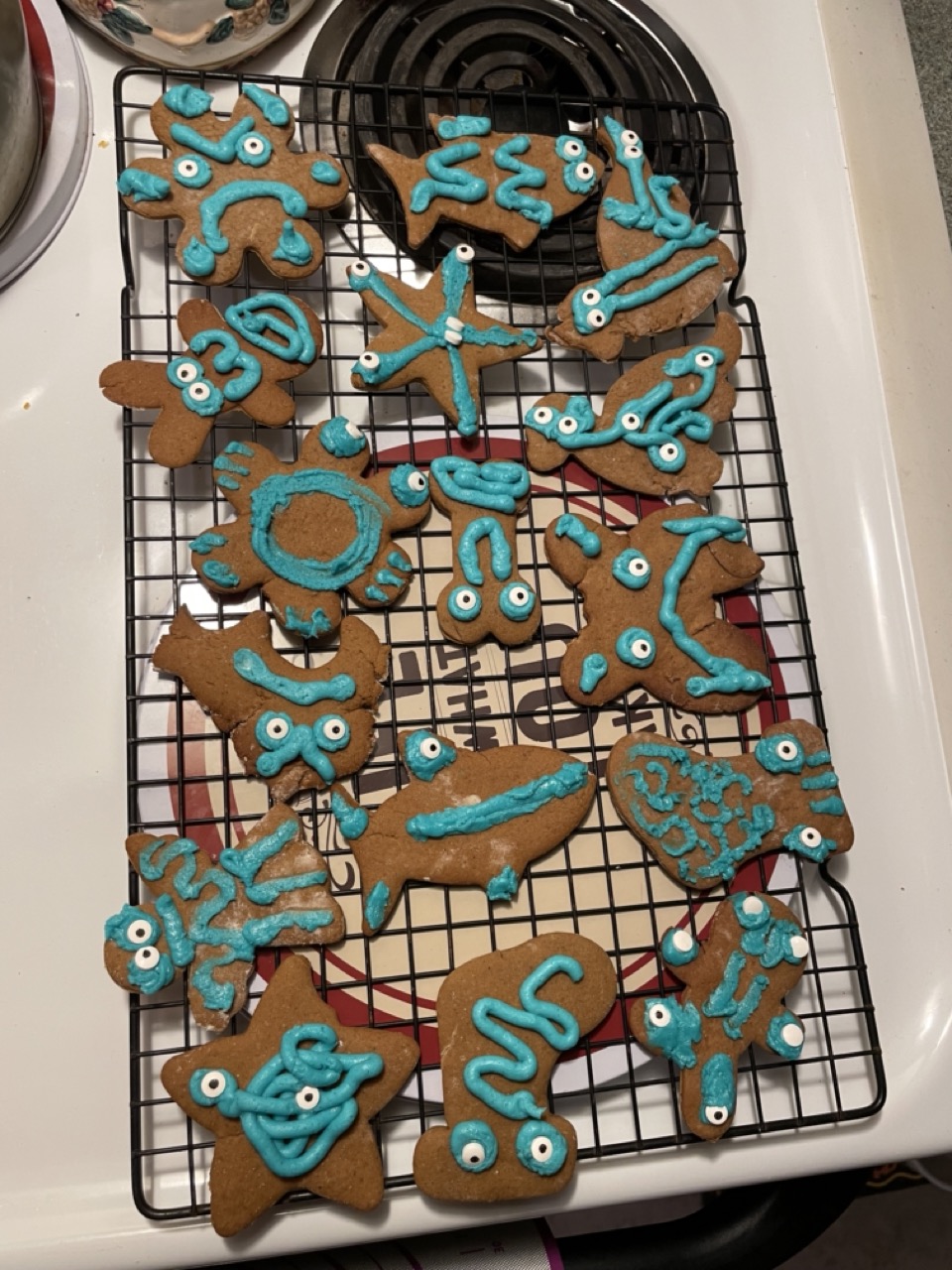 A tray of gingerbread cookies cut into sea-creature shapes and decorated with teal googly-eyed icing.